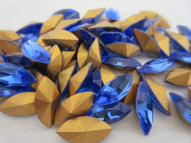 Puede incluir: Un mont&oacute;n de pedrer&iacute;a de cristal azul y dorada. La pedrer&iacute;a tiene forma de marquesa y un dise&ntilde;o facetado.
