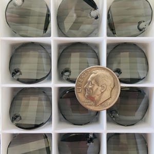 May include: A clear plastic container with 12 round, dark gray crystal beads with a hole in the center. The beads are arranged in a grid pattern. A US dime is included for size reference.