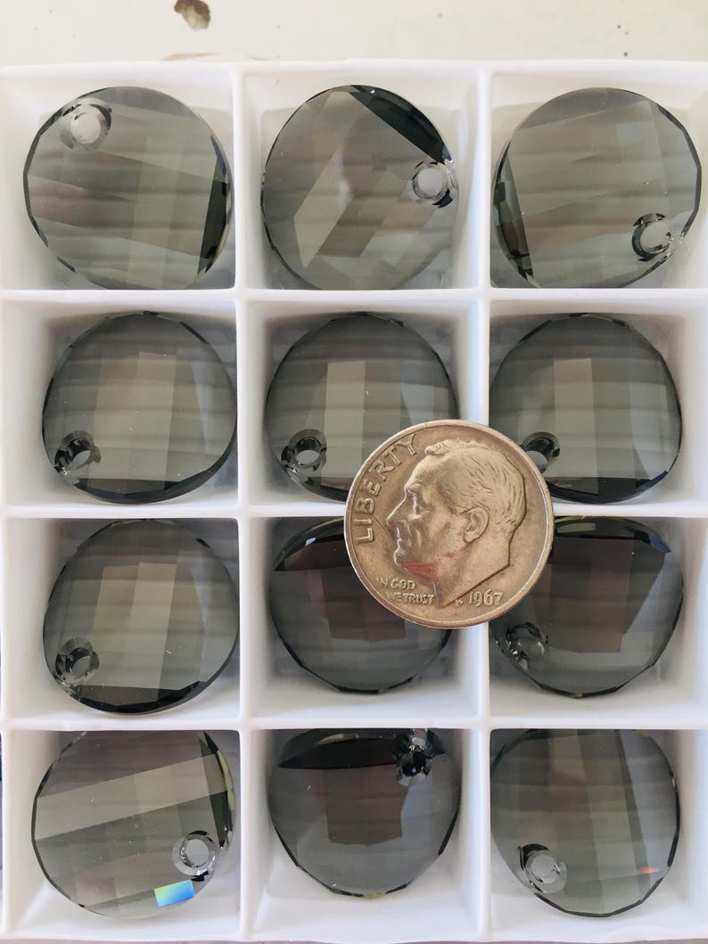 May include: A clear plastic container with 12 round, dark gray crystal beads with a hole in the center. The beads are arranged in a grid pattern. A US dime is included for size reference.