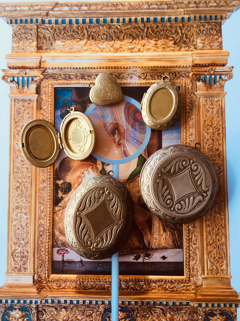 May include: Five gold-toned locket pendants of various shapes and sizes. The lockets are displayed against a background of a framed painting.