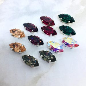 Peut inclure: Une collection de cristaux à facettes en forme de marquise dans diverses couleurs, notamment rouge, vert, violet foncé, brun clair, gris et blanc irisé. Chaque cristal est monté sur un support en métal argenté avec quatre petites griffes.