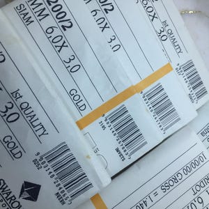 May include: Close-up of three labels for Swarovski crystal beads. The labels are white with black text and barcodes. The labels list the size, color, and quantity of the beads. The text on the labels reads: "4200/2 6.0X 3.0 Amethyst Gold 1440 pcs.", "200/2 6.0X 3.0 Siam Gold", and "4200/2 6.0X Peridot Sapphire 10/00/00 Gross".
