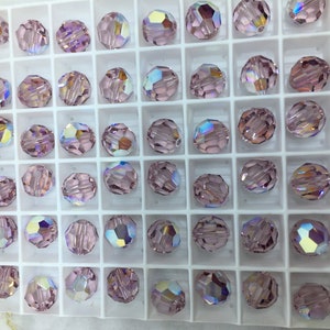 Peut inclure: Vue rapproch&eacute;e d'un plateau de perles de verre de couleur lilas clair. Les perles sont dispos&eacute;es en grille et ont une finition facet&eacute;e et iris&eacute;e.