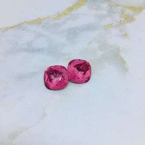 May include: Two pink square-shaped crystal rhinestones.