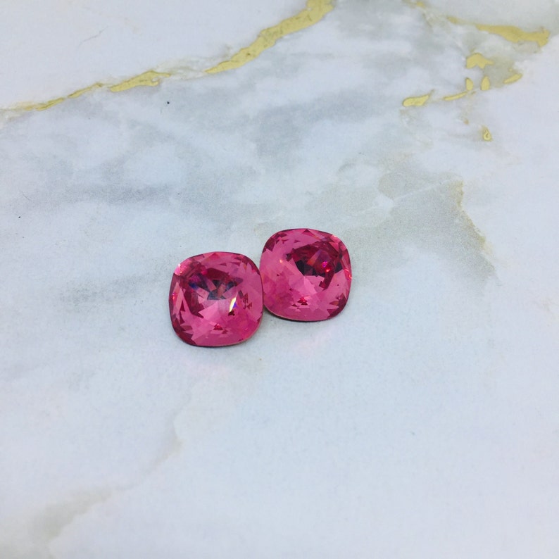 May include: Two pink square-shaped crystal rhinestones.