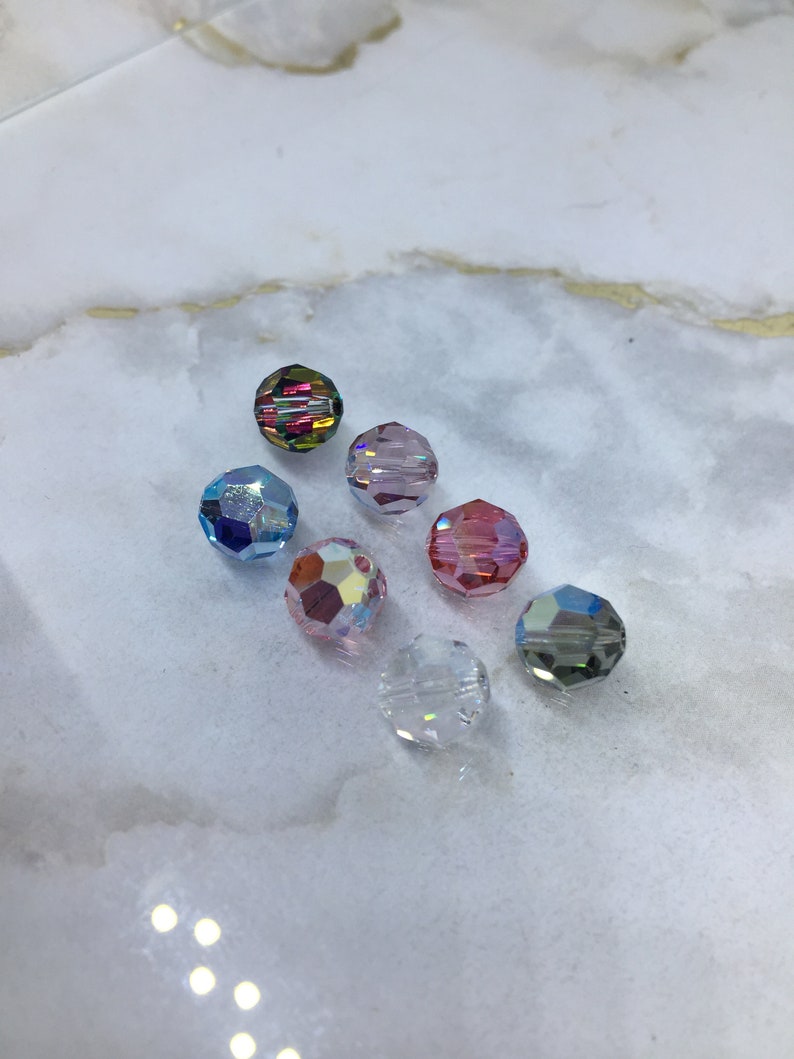 Peut inclure: Assortiment de huit perles de verre facett&eacute;es de diff&eacute;rentes couleurs, notamment transparentes, roses, bleues et iris&eacute;es.