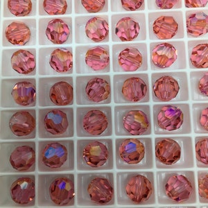 Peut inclure: Une vue rapproch&eacute;e d'un plateau de perles rondes en verre rose. Les perles sont dispos&eacute;es en grille et ont un design facett&eacute;.