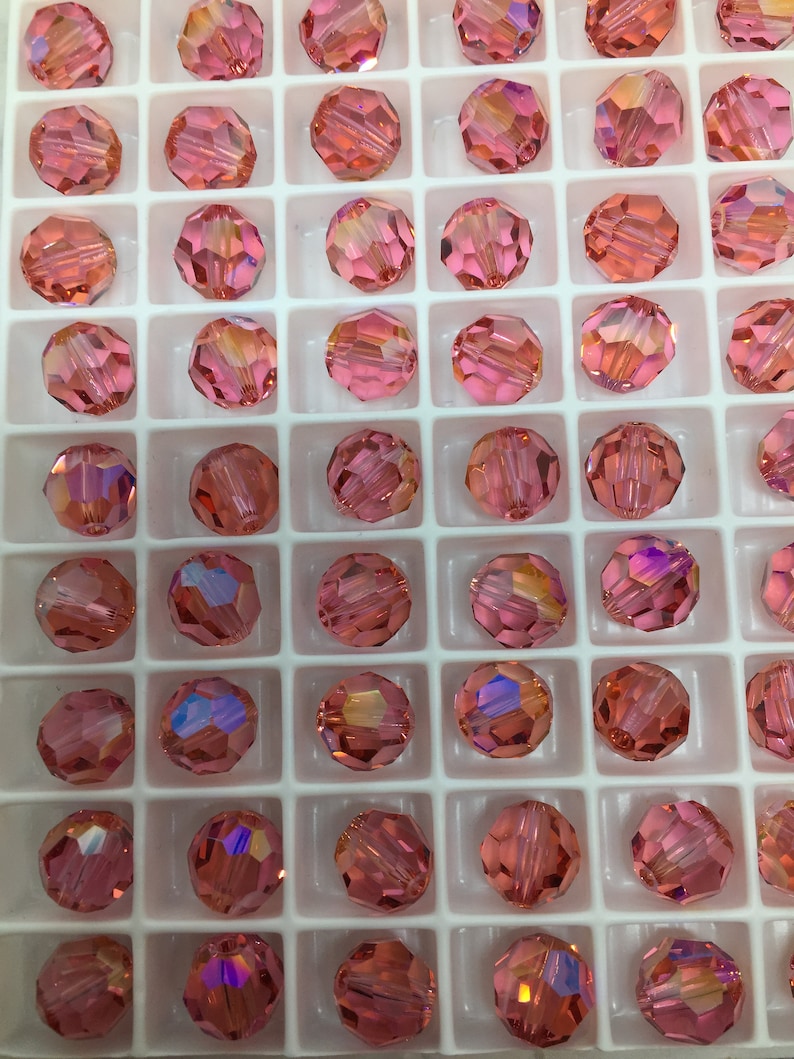 Peut inclure: Une vue rapproch&eacute;e d'un plateau de perles rondes en verre rose. Les perles sont dispos&eacute;es en grille et ont un design facett&eacute;.