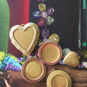 May include: Four gold-toned locket pendants with intricate designs. Two are heart-shaped, one is round, and one is oval. The lockets are open and show the inside of the locket.