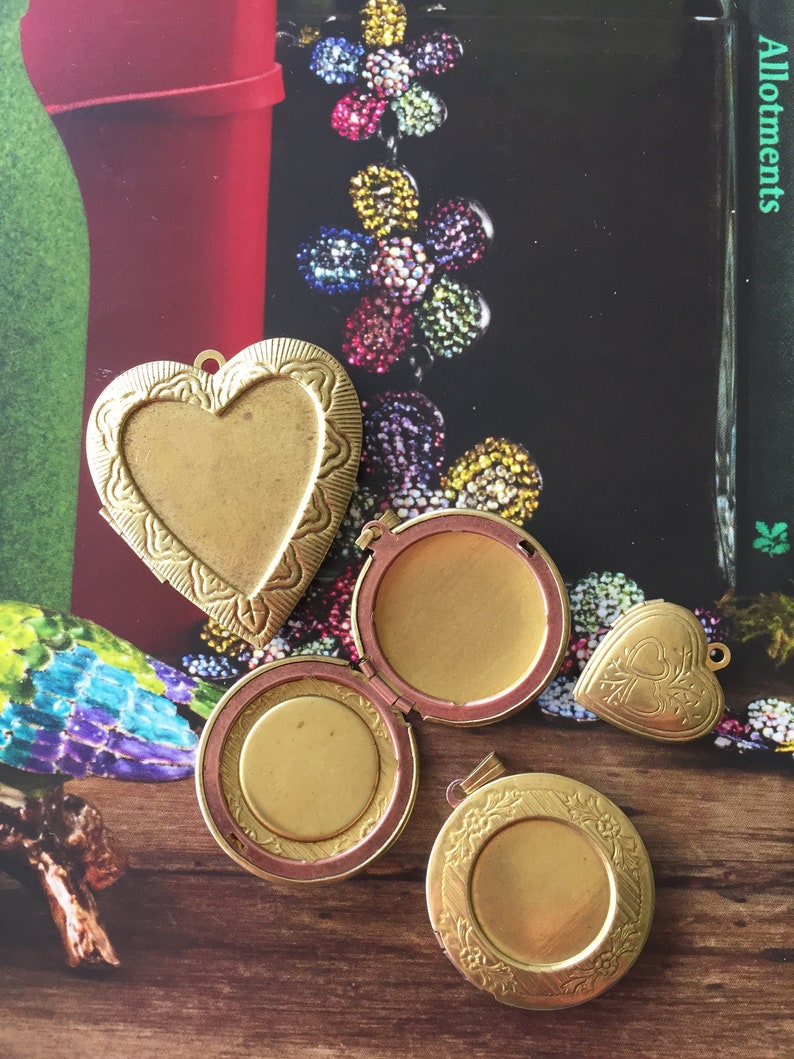 May include: Four gold-toned locket pendants with intricate designs. Two are heart-shaped, one is round, and one is oval. The lockets are open and show the inside of the locket.