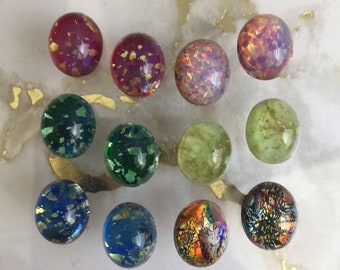 May include: Twelve round glass cabochons with iridescent and metallic finishes. The cabochons are arranged in three rows of four. The colors include pink, red, green, blue, and orange.