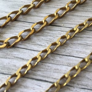 Può includere: Tre catene d'oro di diverse lunghezze, tutte con un design a maglia curb. Le catene sono disposte su una superficie in legno chiaro.