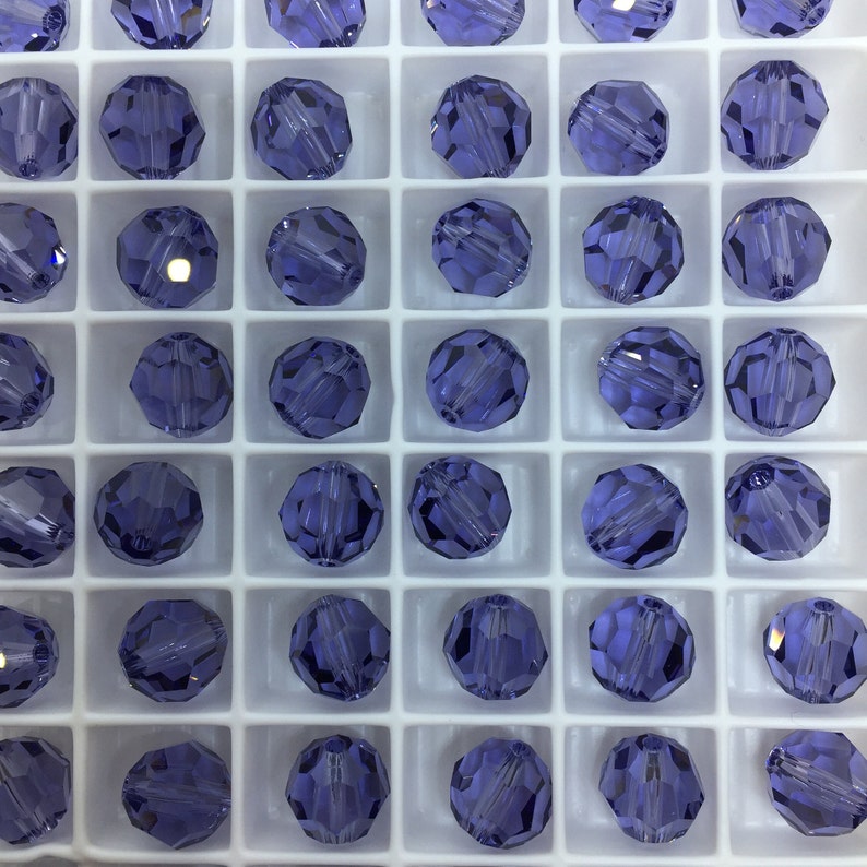 May include: A close-up view of a grid of small, round, purple glass beads. The beads are arranged in a grid pattern and are all the same size and shape.
