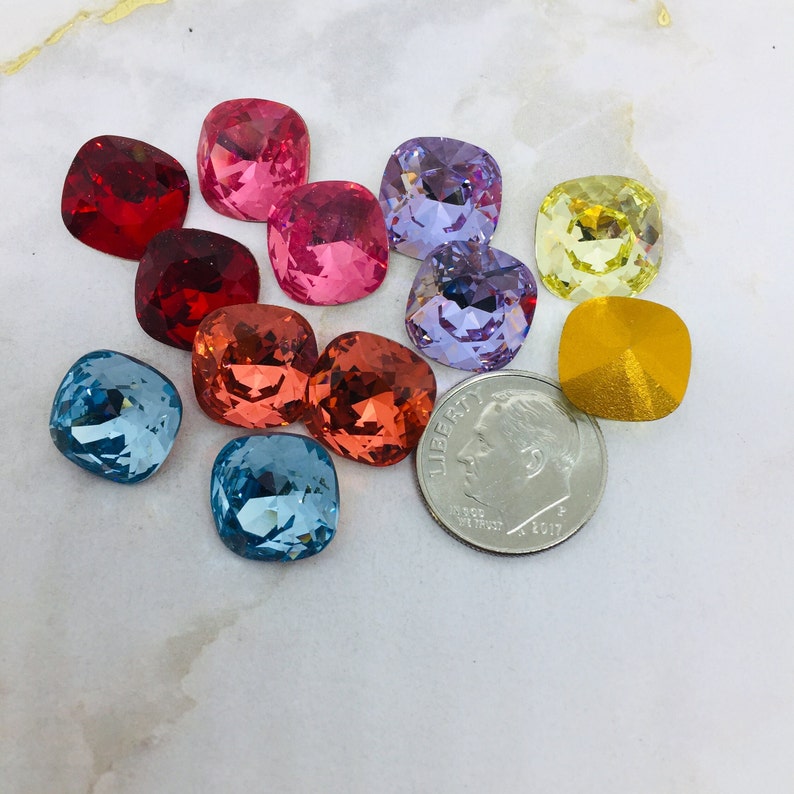 May include: Assortment of colorful square-shaped glass rhinestones in various colors, including red, pink, purple, blue, yellow, and orange. The rhinestones are arranged on a white surface with a US dime for scale.