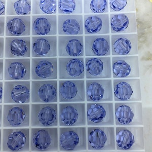 May include: A close-up view of a white plastic tray filled with 49 light blue glass beads. The beads are arranged in a grid pattern.