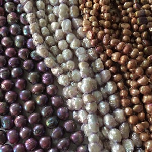 May include: Three strands of pearl necklaces, one strand is dark purple, one is light purple, and one is brown. The pearls are all of different sizes and shapes.