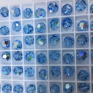 Peut inclure: Gros plan d'un r&eacute;cipient rempli de perles rondes en verre bleu clair. Les perles sont dispos&eacute;es en grille et ont un design facett&eacute;.