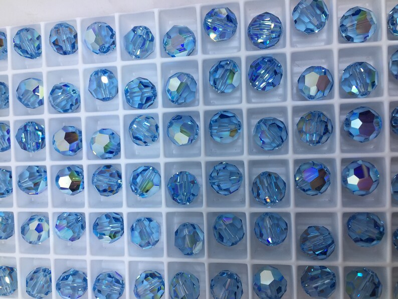 Peut inclure: Gros plan d'un r&eacute;cipient rempli de perles rondes en verre bleu clair. Les perles sont dispos&eacute;es en grille et ont un design facett&eacute;.