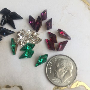 May include: Assortment of colorful rhinestones in various shapes and sizes, including black, green, red, and purple. A US dime is included for scale.