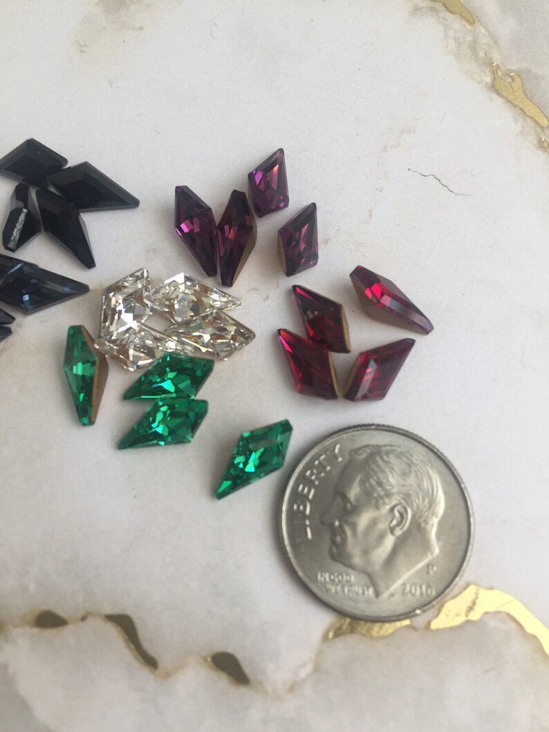 May include: Assortment of colorful rhinestones in various shapes and sizes, including black, green, red, and purple. A US dime is included for scale.
