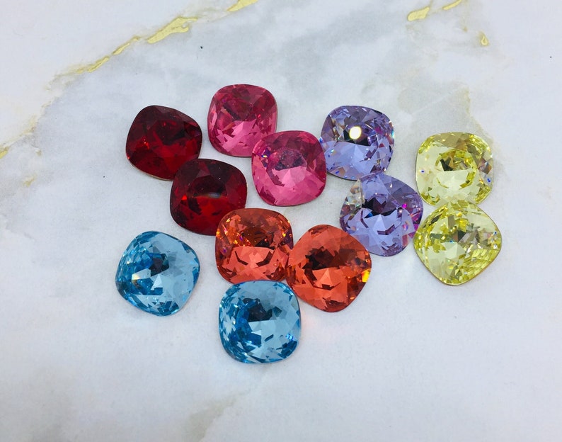 May include: Assortment of colorful square-shaped glass rhinestones. The rhinestones are in shades of red, pink, blue, yellow, and purple.