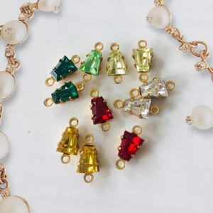 May include: Assortment of colourful glass and crystal connector charms with gold-tone metal settings. The charms feature a variety of colours, including red, green, yellow, and clear.