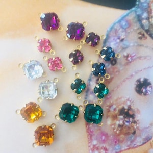 May include: A collection of colorful square and flower-shaped crystal rhinestones with gold-colored connectors. The crystals are in shades of purple, pink, clear, orange, and green. These decorative rhinestones are ideal for jewelry making and craft projects.