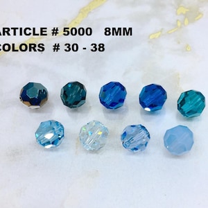 May include: Nine faceted round beads in various shades of blue, ranging from dark teal to light sky blue. The text ARTICLE # 5000 8MM and COLORS # 30 - 38 is printed above the beads. Each bead features a multi-faceted surface that reflects light.