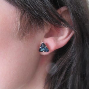 Può includere: Un paio di orecchini a forma triangolare con una pietra preziosa blu scuro.