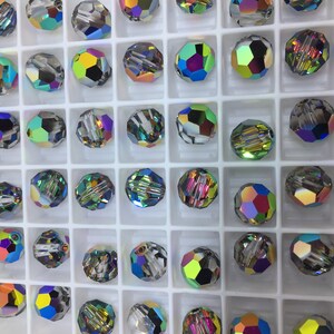 Peut inclure: Une vue rapproch&eacute;e d'un plateau de perles de verre iris&eacute;es. Les perles sont dispos&eacute;es en grille et sont toutes de diff&eacute;rentes nuances de bleu, vert et violet.