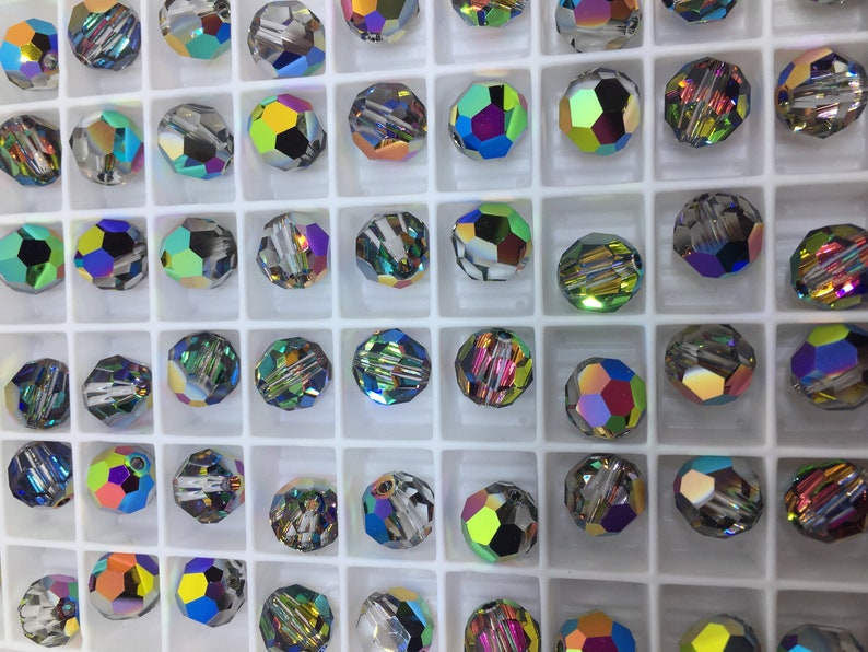 Peut inclure: Une vue rapproch&eacute;e d'un plateau de perles de verre iris&eacute;es. Les perles sont dispos&eacute;es en grille et sont toutes de diff&eacute;rentes nuances de bleu, vert et violet.