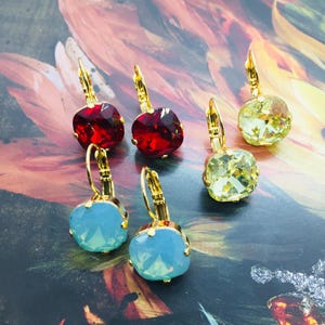 Puede incluir: Un conjunto de seis pendientes de tono dorado con piedras de cristal de diferentes colores. Los pendientes presentan una piedra en forma de lágrima con un diseño facetado. Las piedras son rojas, amarillas y azules.