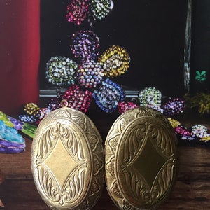 May include: Two gold oval-shaped lockets with intricate floral designs. The lockets are closed and have a shiny finish.