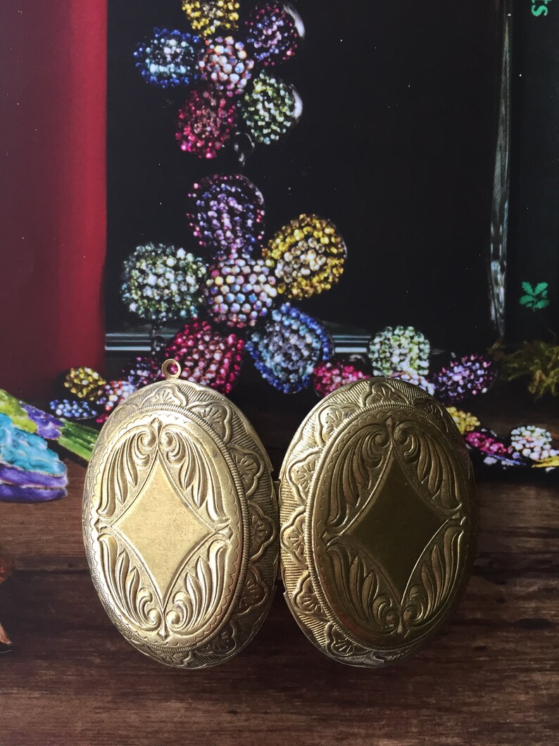 May include: Two gold oval-shaped lockets with intricate floral designs. The lockets are closed and have a shiny finish.