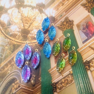 May include: A collection of oval-shaped pendants in various colors, including blue, green, and pink, with gold-colored loops. The pendants are arranged on a background with a church-like design.