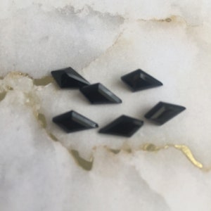 May include: Six black diamond-shaped rhinestones on a white marble surface.
