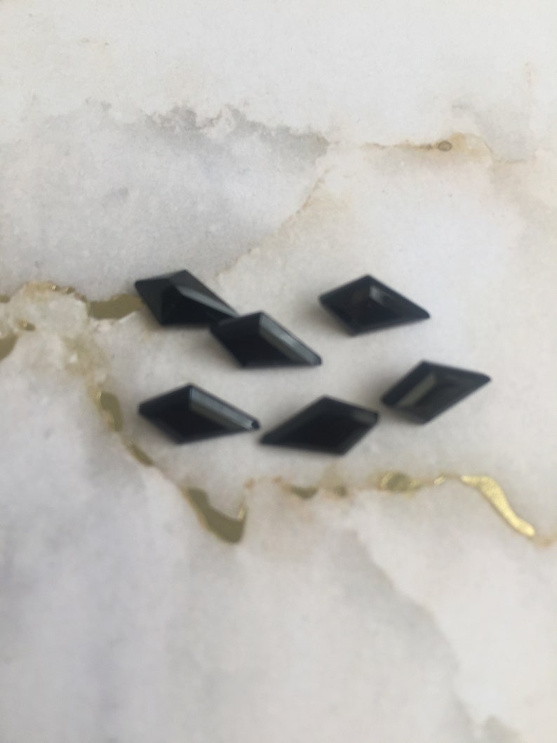 May include: Six black diamond-shaped rhinestones on a white marble surface.