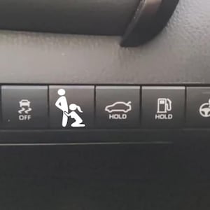 May include: A row of black rectangular vehicle dashboard buttons. The buttons feature white icons including high beams, traction control off, a graphic of two figures, a trunk hold, a fuel door hold, and a heated steering wheel icon.