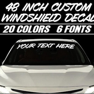 May include: A white custom 48 inch windshield decal with the text "YOUR TEXT HERE" on a car windshield. The decal is available in 20 colors and 6 fonts.