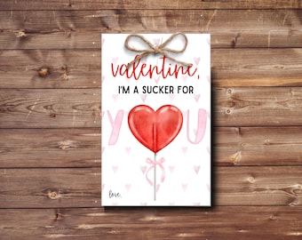 May include: Valentine's Day card with a red heart lollipop and the text "valentine, I'm a sucker for you". The background is white with pink hearts.