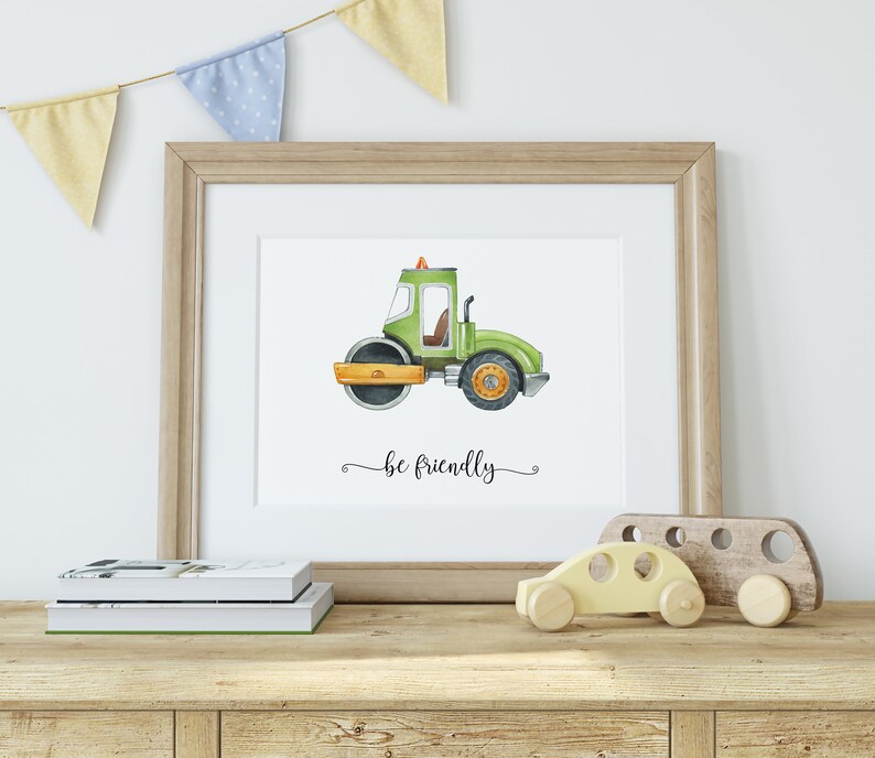 Op de afbeelding: Een aquarel-illustratie van een groen bouwvoertuig met de tekst "be friendly" eronder. De illustratie is ingelijst in een licht houten lijst en wordt tentoongesteld op een plank met een houten speelgoedauto.