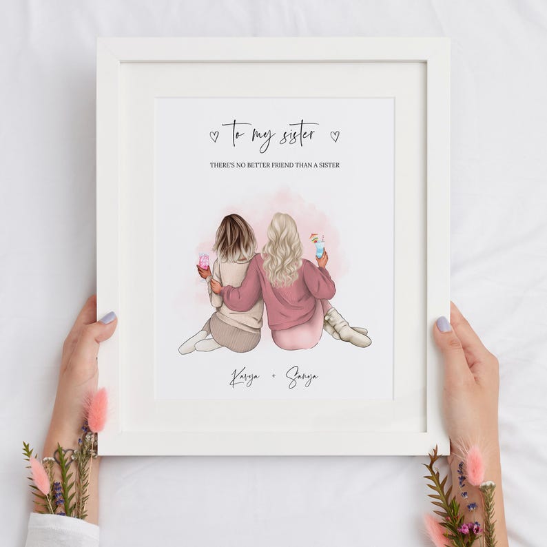 May include: A white framed print with a pink and white illustration of two women holding drinks. The text reads "To my sister" and "There's no better friend than a sister". The names "Karisa" and "Saraya" are written below the illustration.