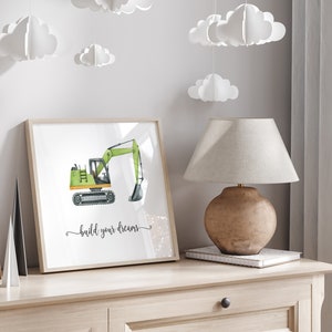 Op de afbeelding: Een ingelijst print met een aquarel-illustratie van een groene graafmachine met de tekst "build your dreams" eronder.
