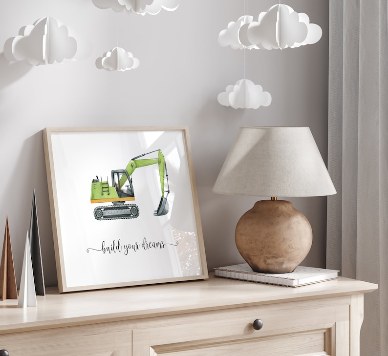 Op de afbeelding: Een ingelijst print met een aquarel-illustratie van een groene graafmachine met de tekst "build your dreams" eronder.