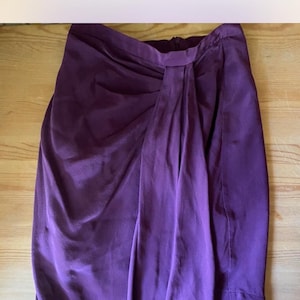 May include: A purple wrap skirt made of a silky fabric. The skirt has a simple design and is a versatile piece of clothing.