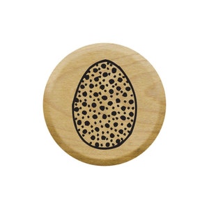 May include: A round wooden stamp with a black and white design of an egg with a speckled pattern.