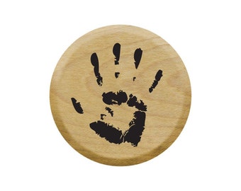 Op de afbeelding: Een ronde houten knoop met een zwarte handafdruk.