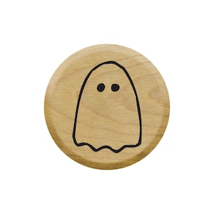 Pode incluir: Um botão redondo de madeira com um contorno preto de um fantasma com dois olhos.