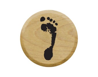 Op de afbeelding: Een ronde houten stempel met een zwart voetafdruk ontwerp.