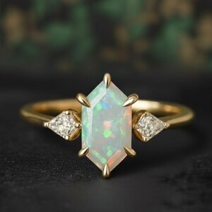 Könnte beinhalten: Ein goldener Ring mit einem großen, schillernden Opal-Edelstein in sechseckiger Form. Der Ring hat zwei kleine, dreieckige Diamant-Akzente. Das Band ist aus poliertem Gold.